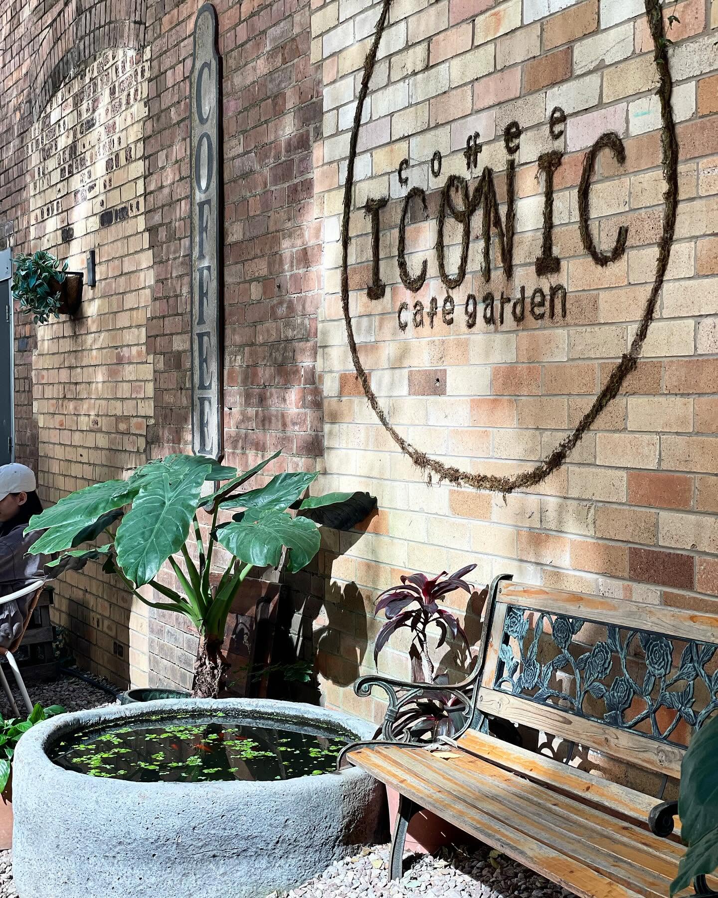 Jardín de Coffee Iconic con muro de ladrillo, musgo y estanque