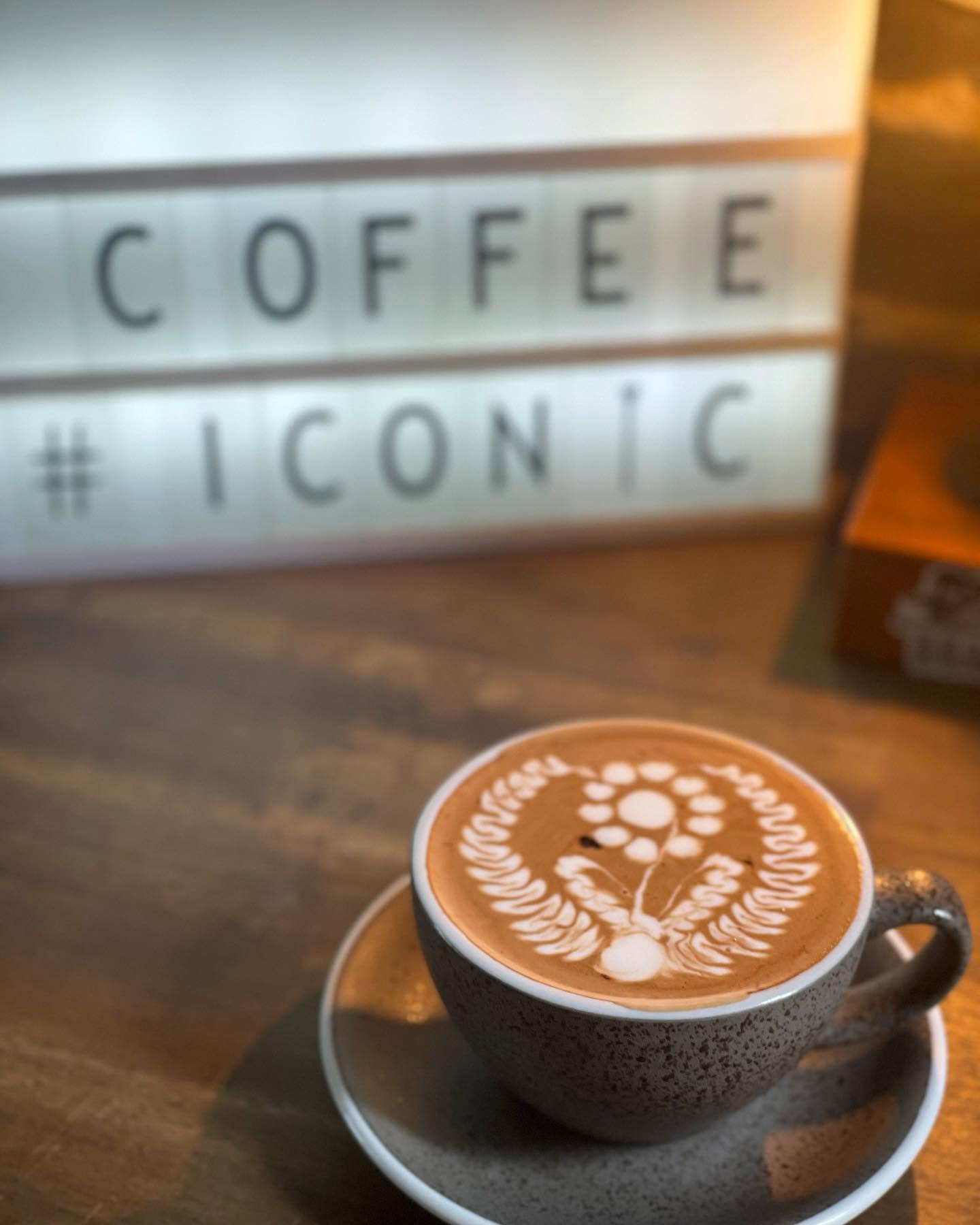 Taza con arte latte floral y cartel luminoso COFFEE #ICONIC de fondo
